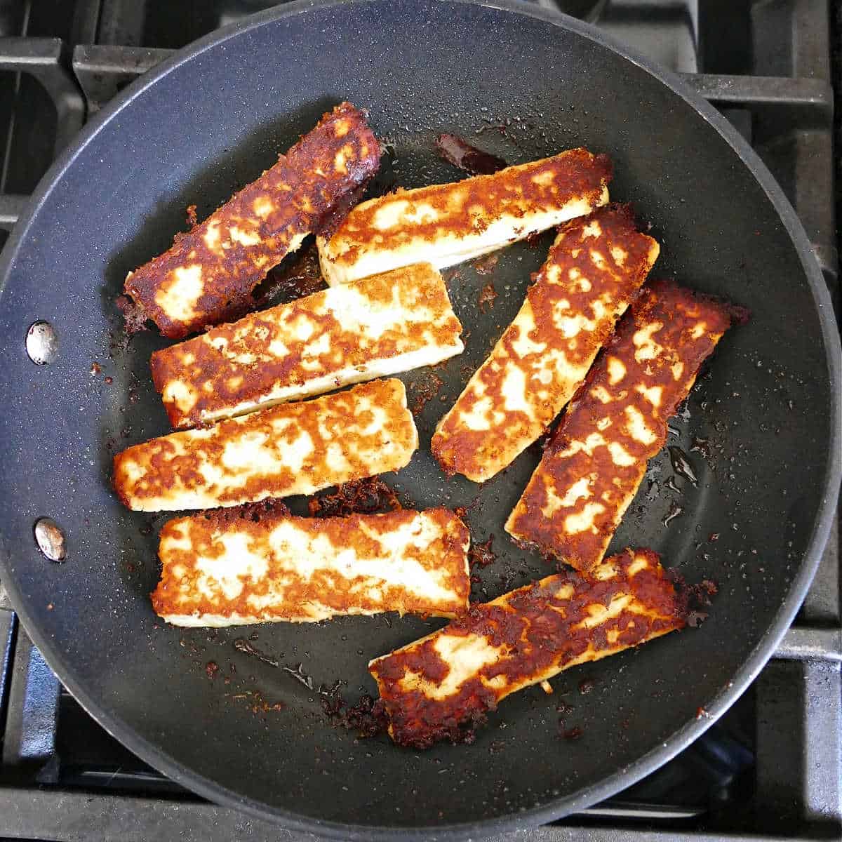 halloumi cheese frying in olive oil and cumin in a skillet on a stove
