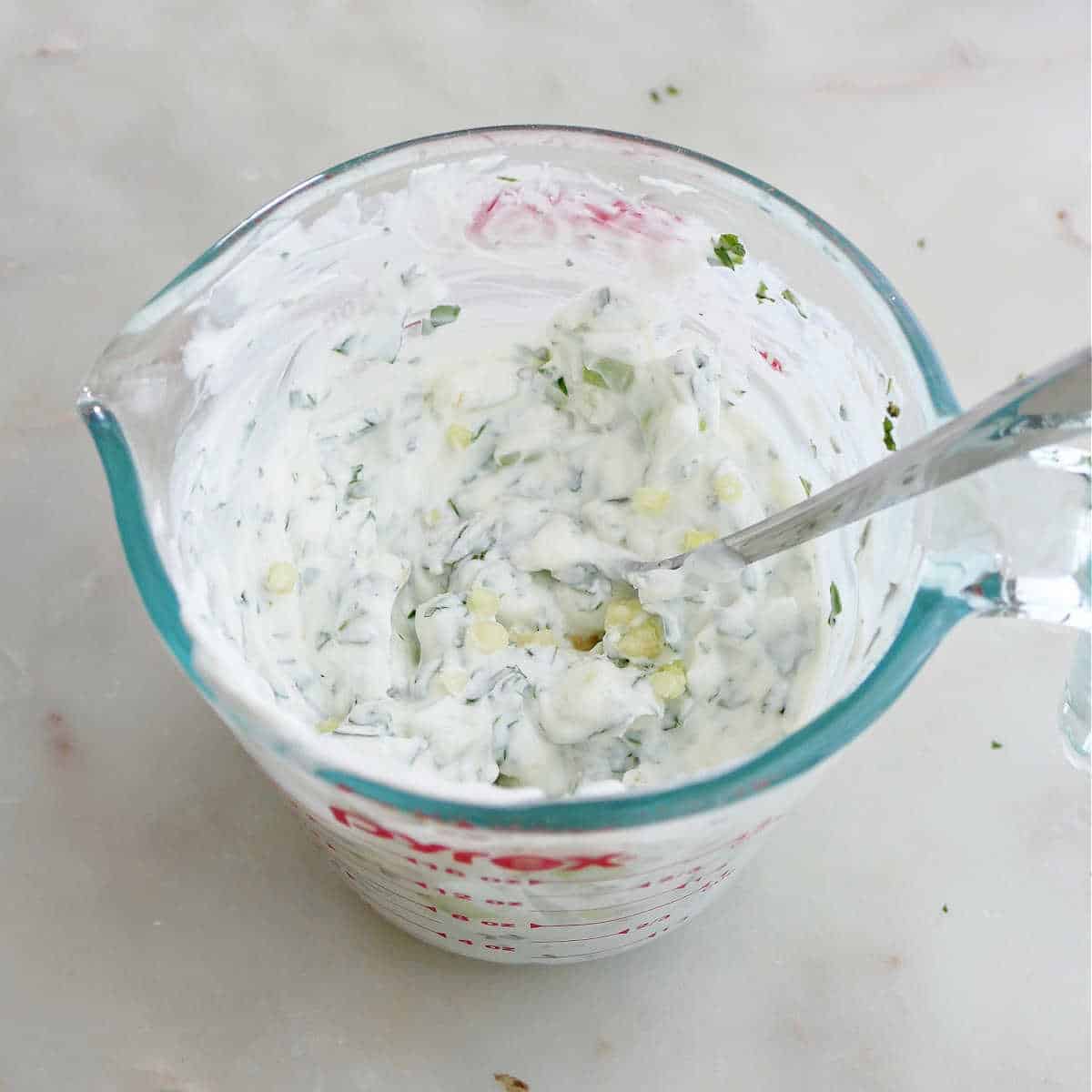 yogurt being mixed with herbs, garlic, and lemon juice in a measuring cup