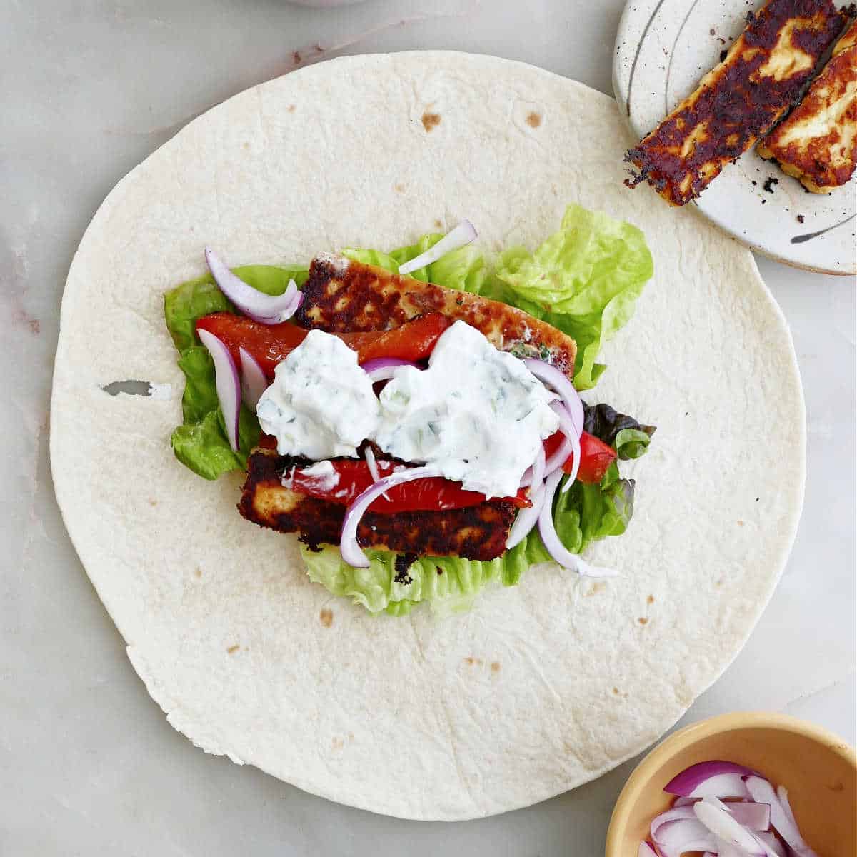 halloumi and vegetables with yogurt sauce on a tortilla before being rolled into a wrap