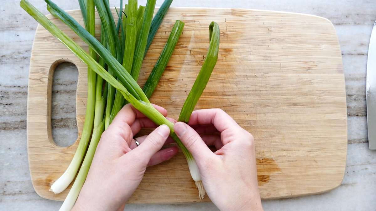 woman removing wilted leaves from a scallion over a cutting board