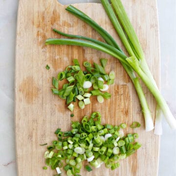 sliced green onions next to whole ones on a cutting board