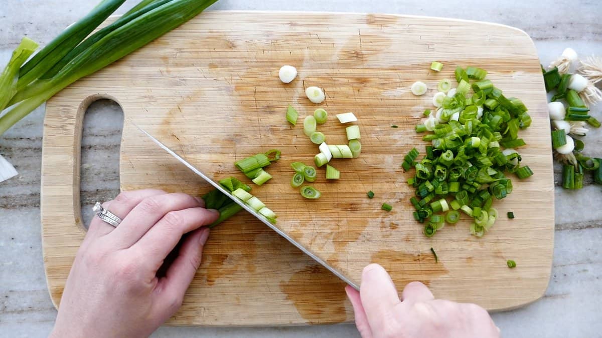 woman slicing green onions on a diagonal on a cutting board