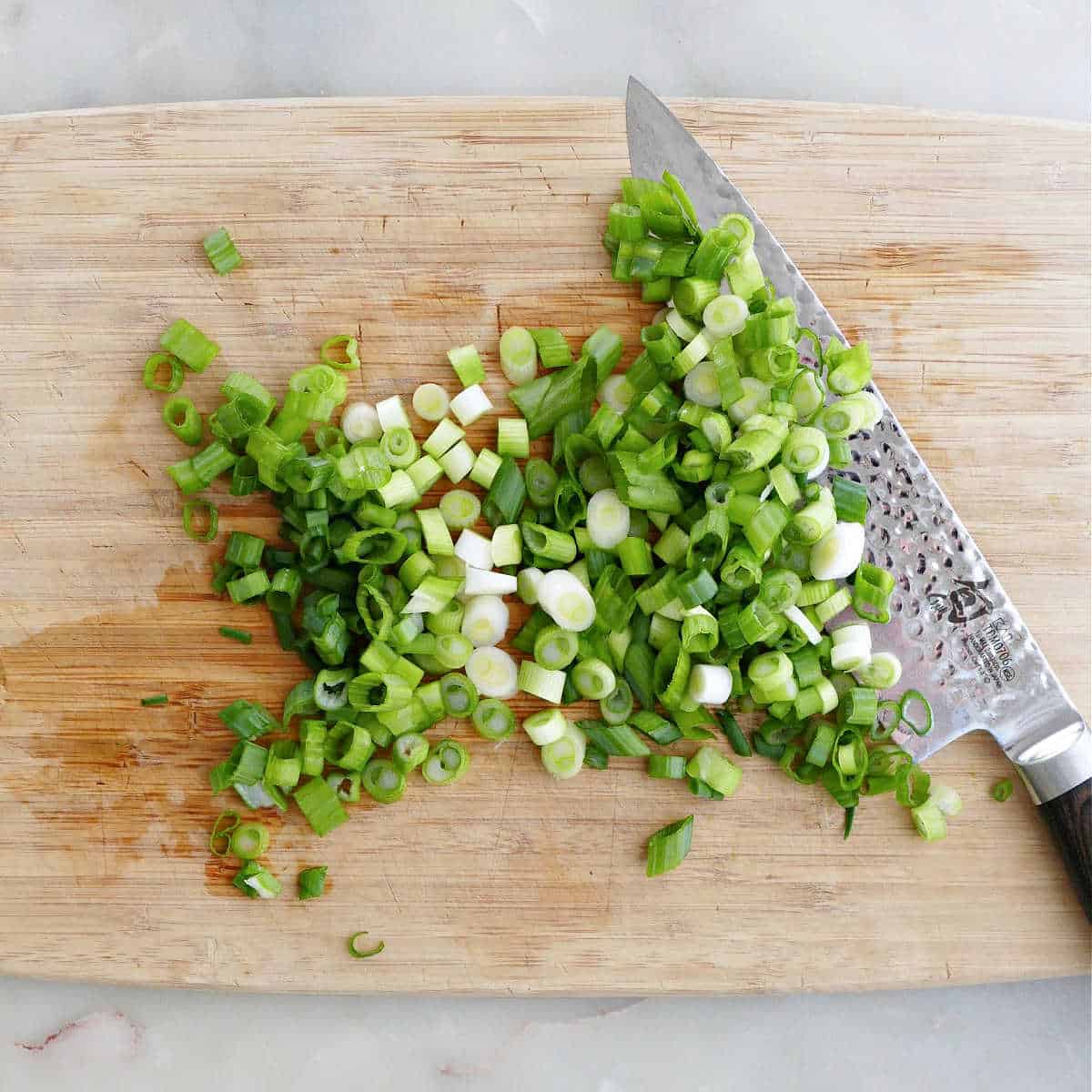 sliced green onions on a cutting board next to a chef's knife