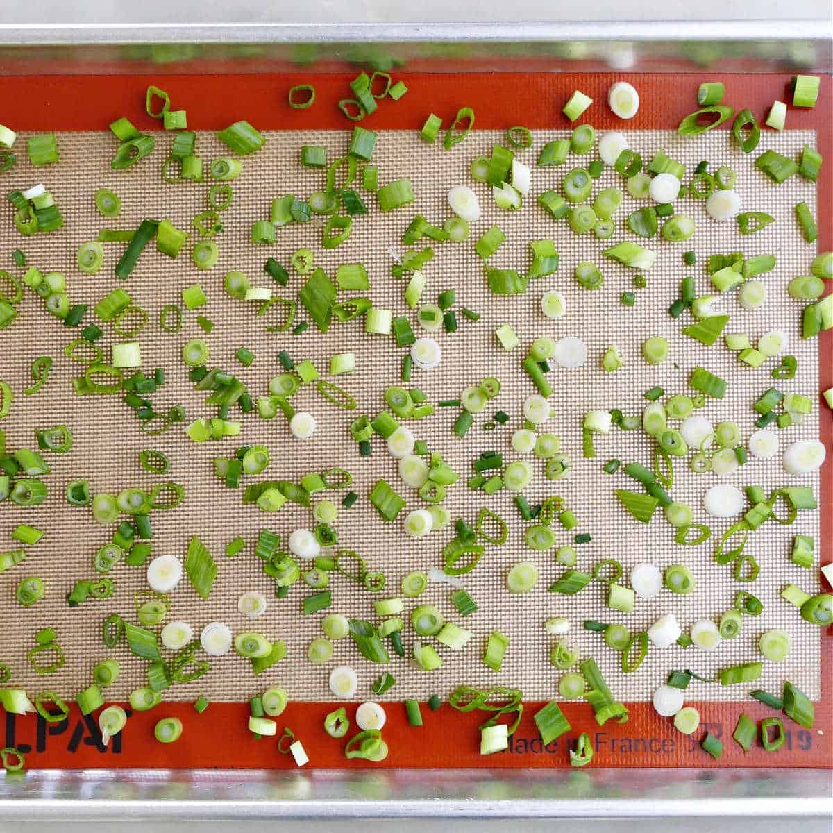 green onions spread out on a lined baking sheet before being frozen