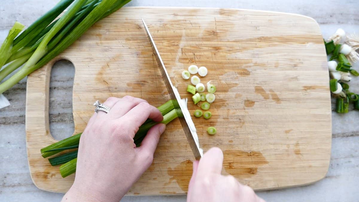 woman slicing green onions into pieces on a cutting board