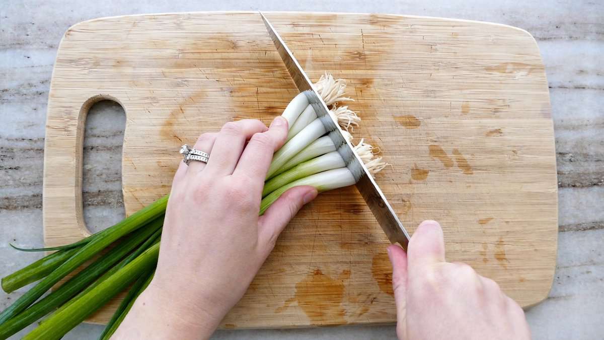 woman trimming the stringy ends off of scallions on a cutting board