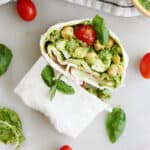pesto chickpea wrap sliced in half on a counter surrounded by ingredients