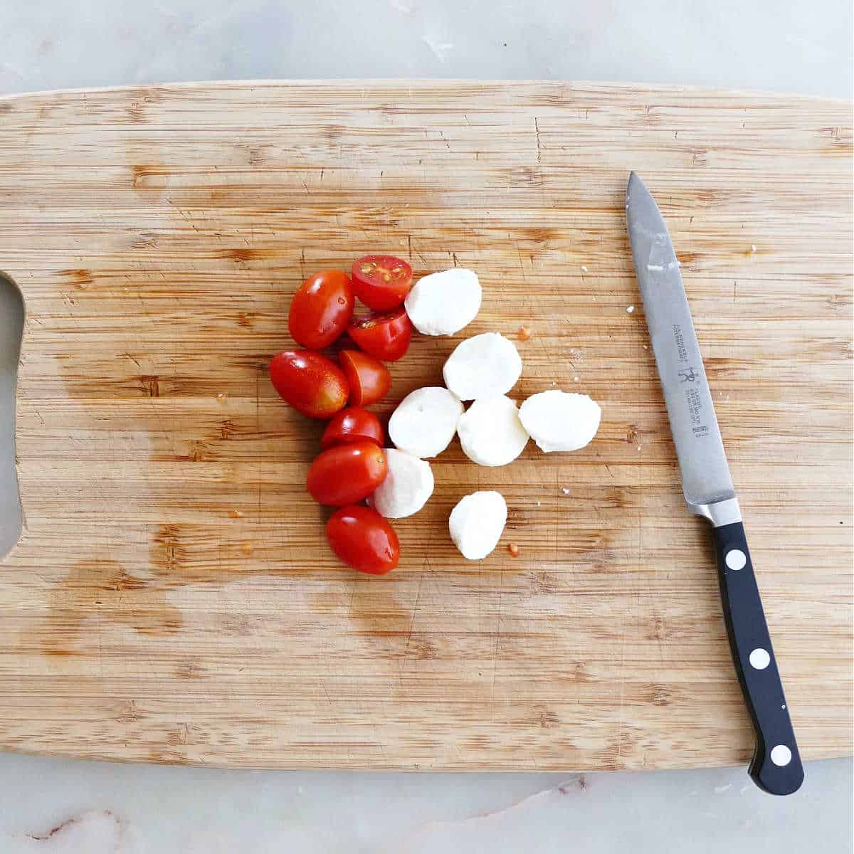 grape tomatoes and mozzarella balls sliced in half on a cutting board
