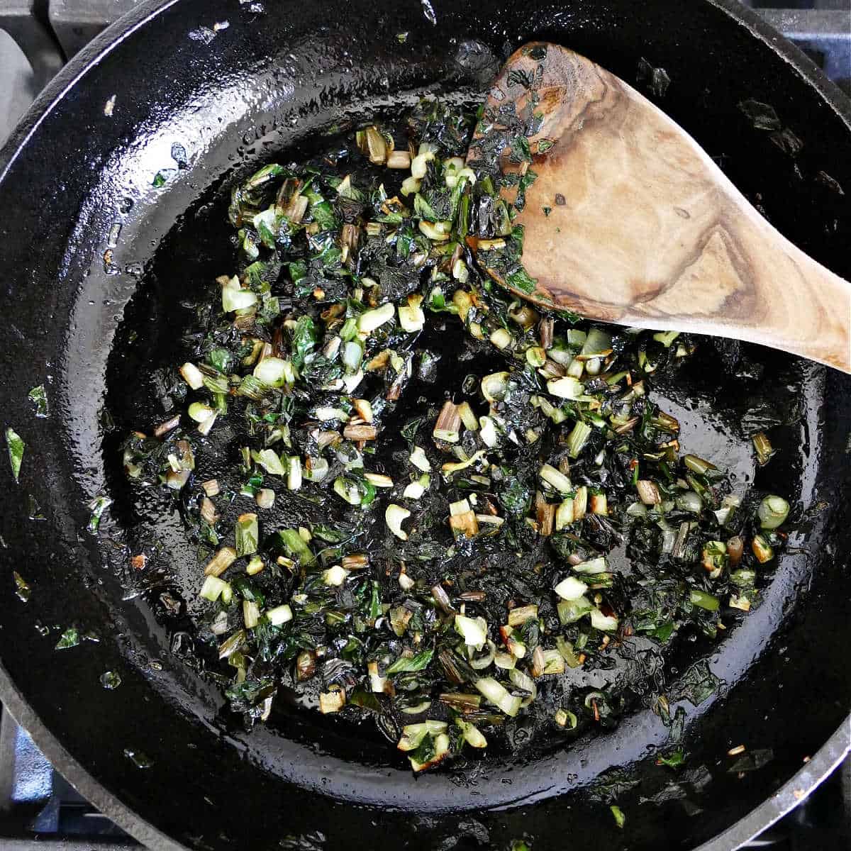chopped ramps cooking in olive oil in a cast iron skillet with a spoon