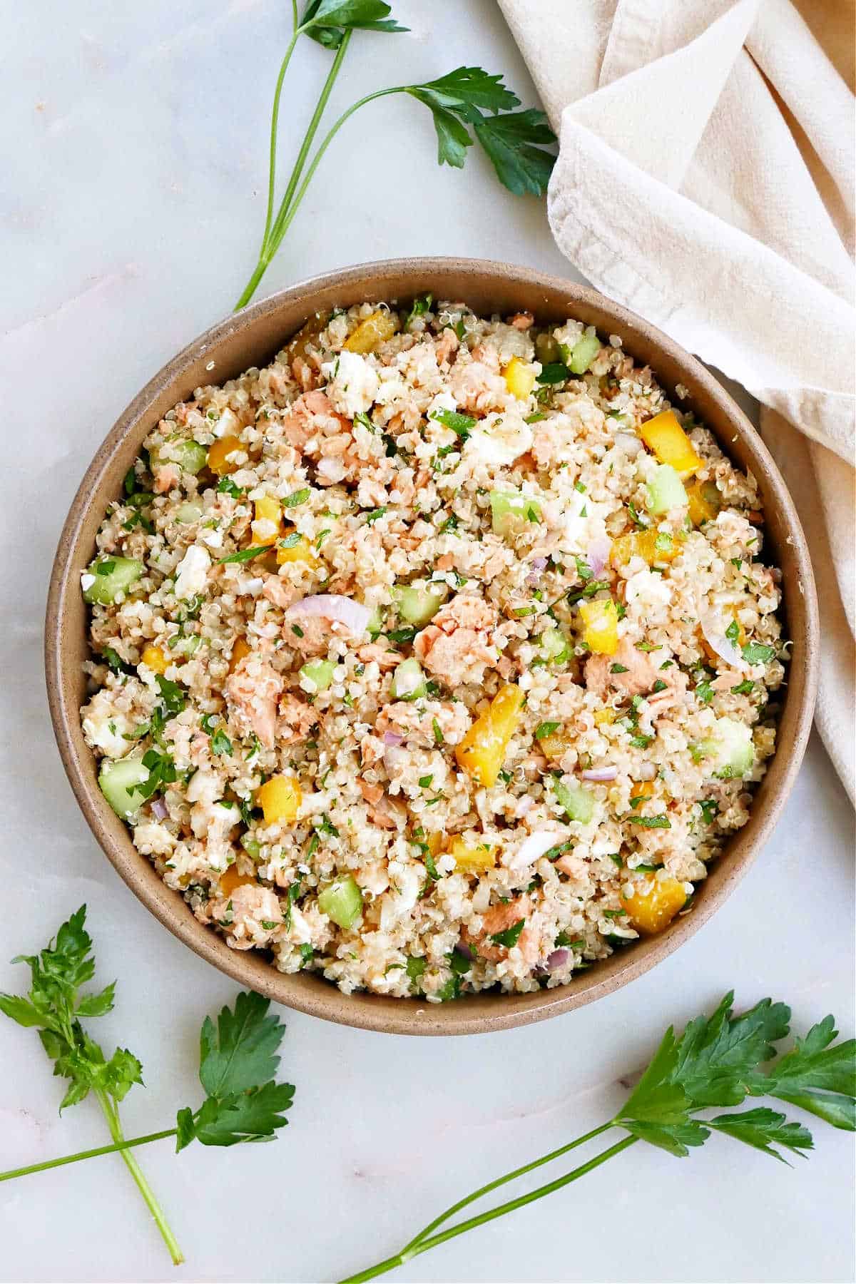 salmon quinoa salad in a serving bowl on a counter next to herbs and napkin