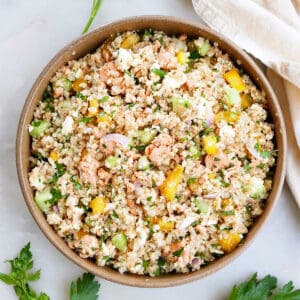 salmon quinoa salad in a serving bowl on a counter next to herbs and napkin