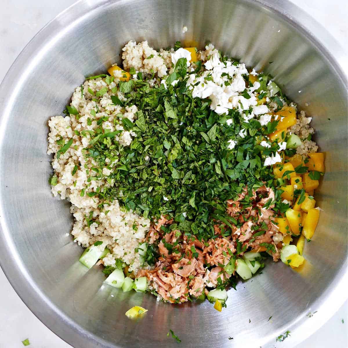 ingredients for quinoa and canned salmon salad in a mixing bowl on a counter