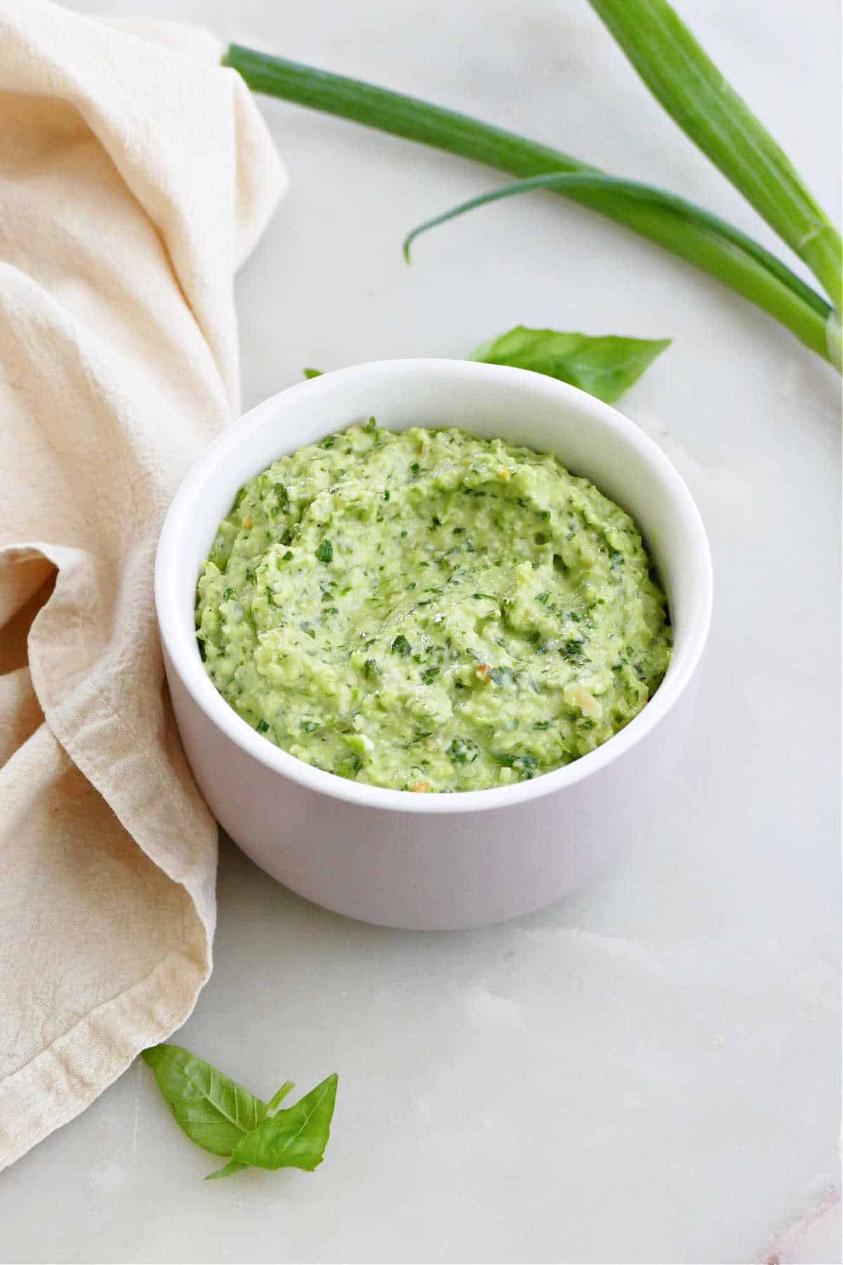 scallion pesto in a bowl surrounded by basil, green onions, and a napkin