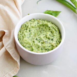 scallion pesto in a bowl surrounded by basil, green onions, and a napkin