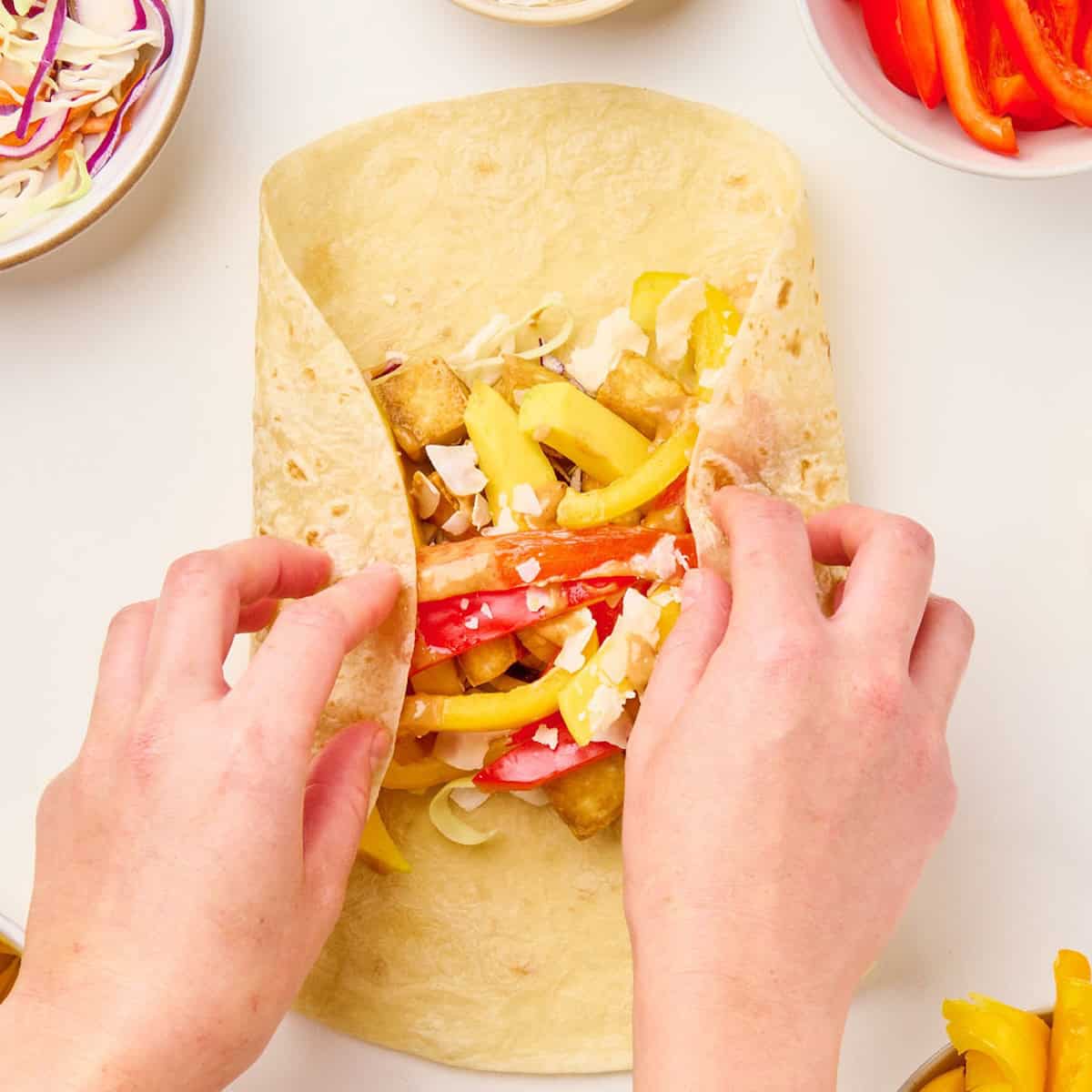 Woman folding the edges of a tortilla over the fillings to make a wrap.