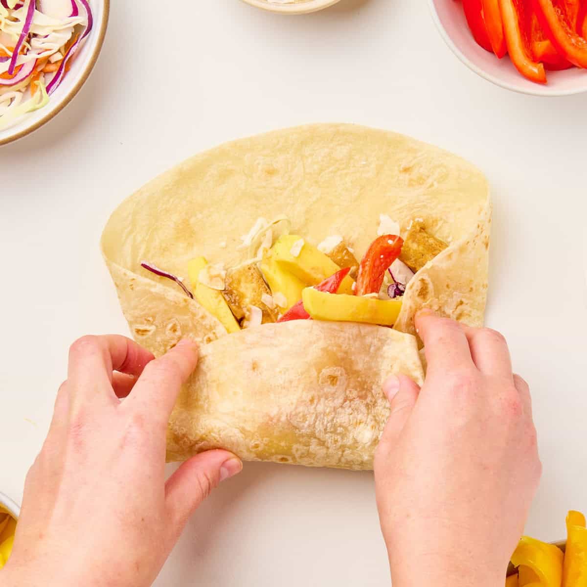 Woman rolling a tortilla from the bottom to make a tofu wrap.