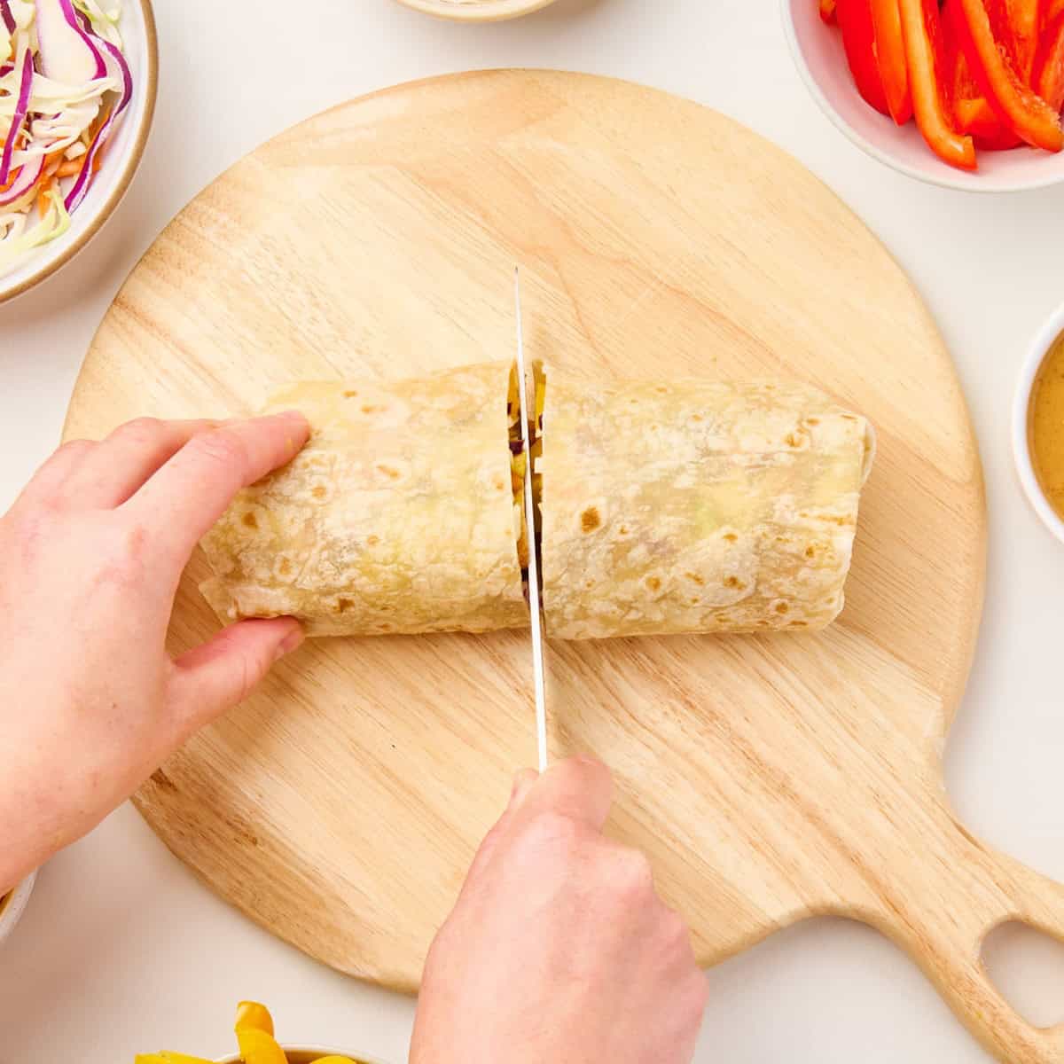 Woman slicing a tofu wrap into two halves with a knife on a cutting board.