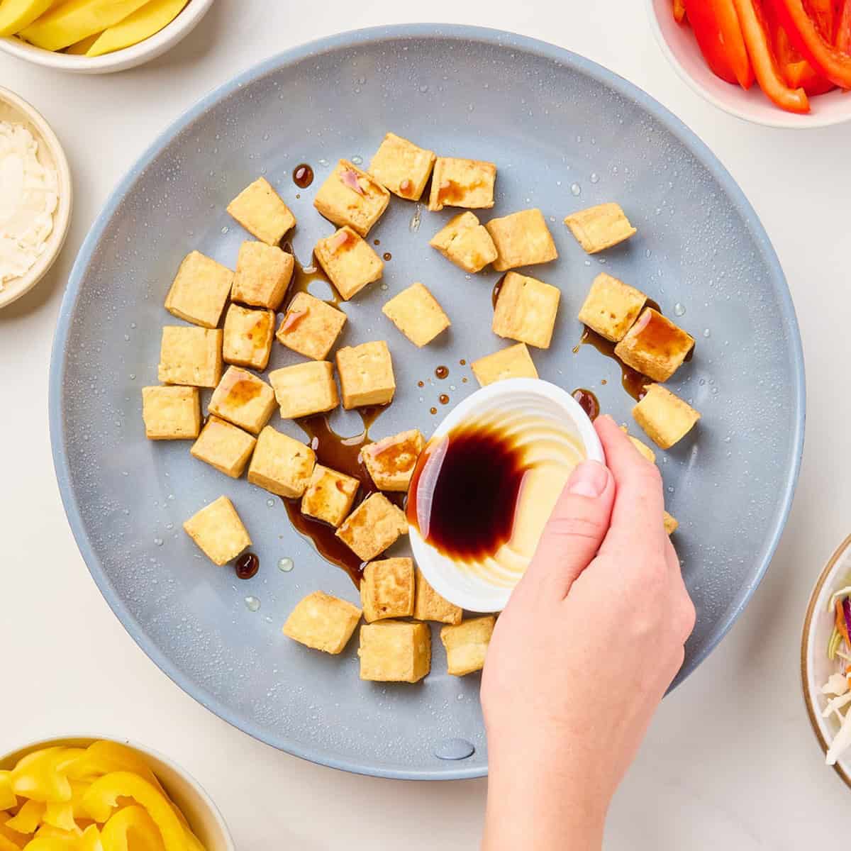 Woman pouring soy sauce into a skillet of fried tofu.