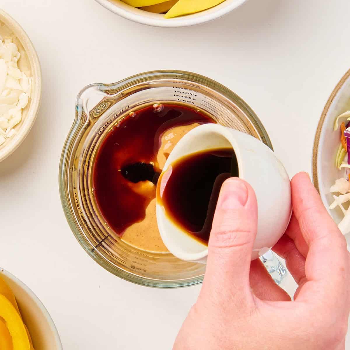 Woman pouring soy sauce into a measuring cup with peanut butter.