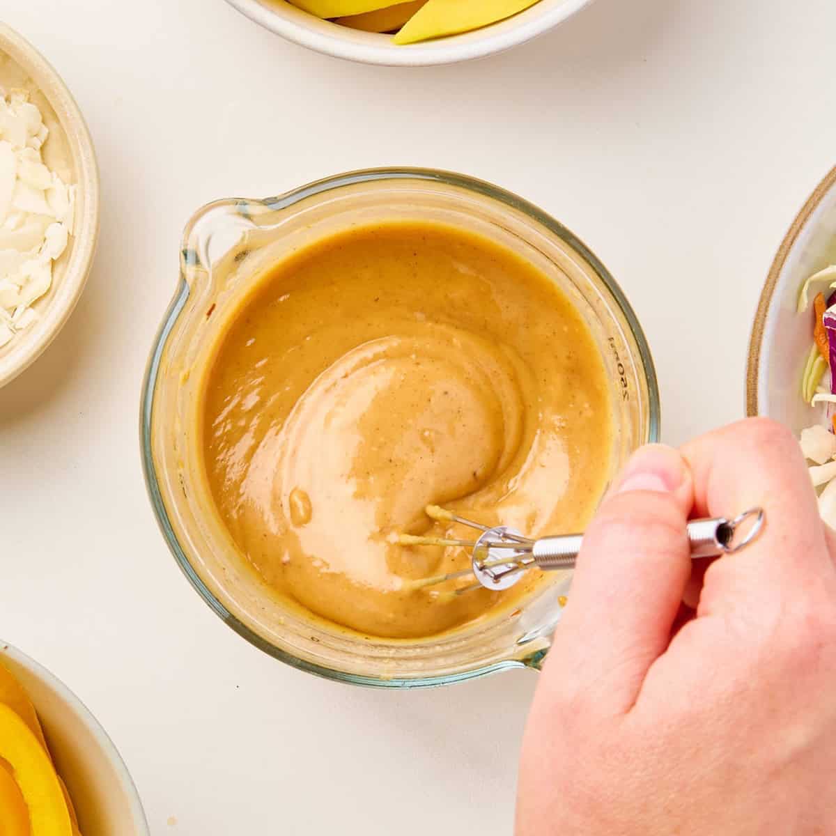 Woman whisking peanut sauce for tofu wraps in a measuring cup.