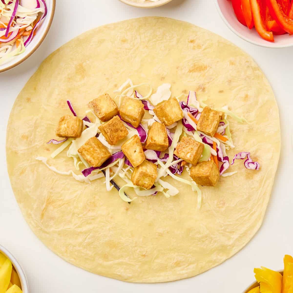 Coleslaw mix and tofu on a flour tortilla on a counter.