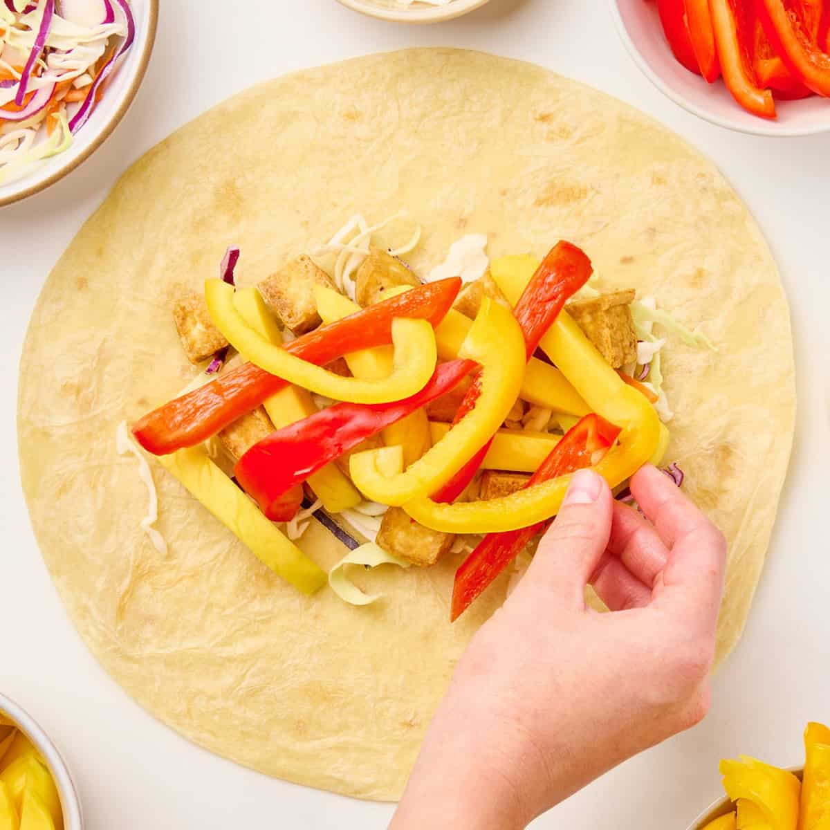 Woman adding peppers and mango to a tortilla with tofu.