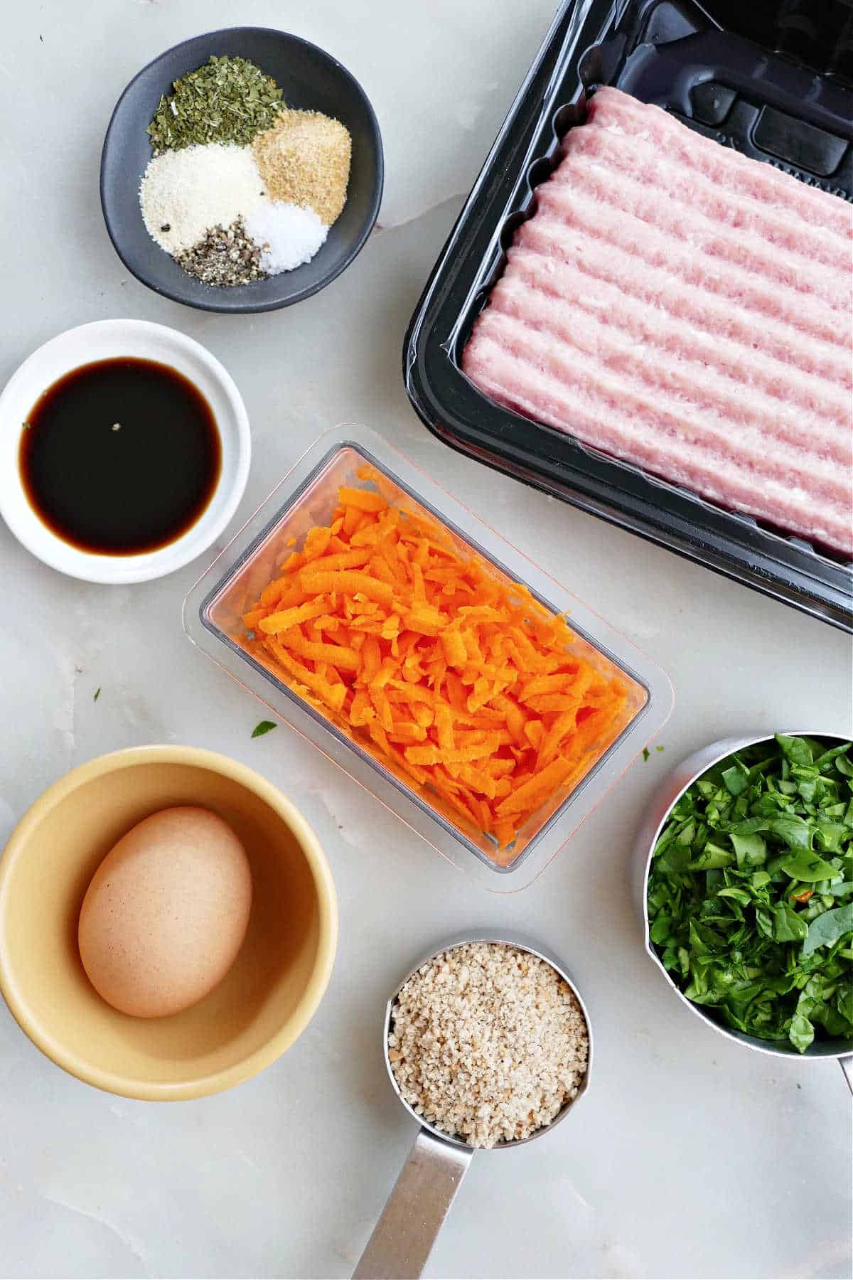 ground chicken, seasonings, chopped spinach, shredded carrots, breadcrumbs, egg, and Worcestershire on a counter