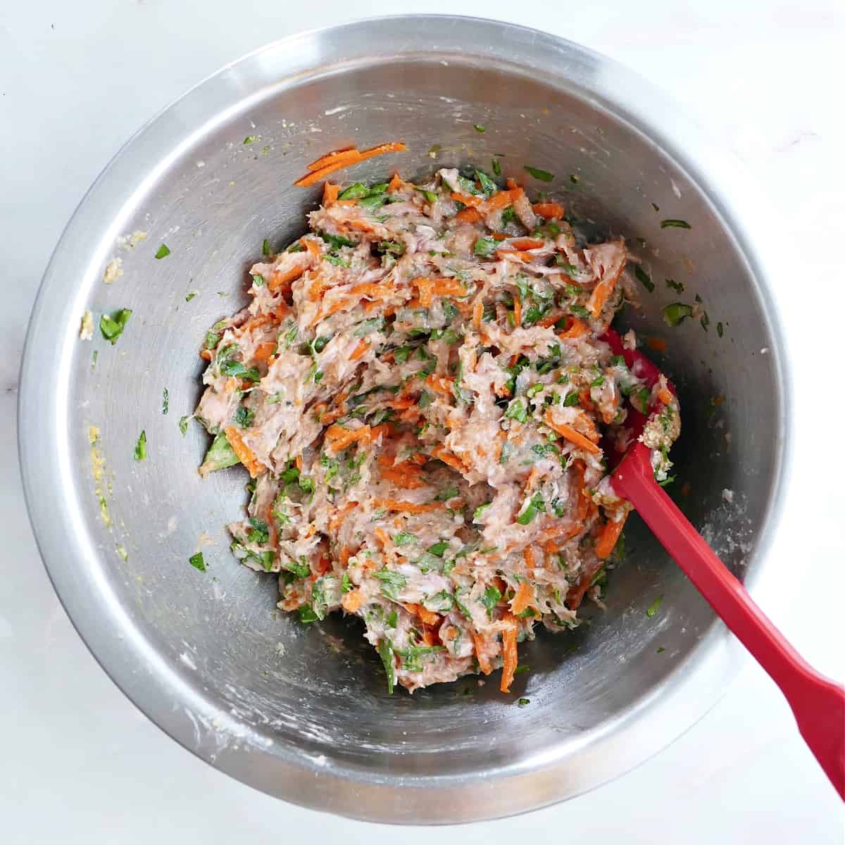 ground chicken mixed together with veggies and seasonings in a mixing bowl