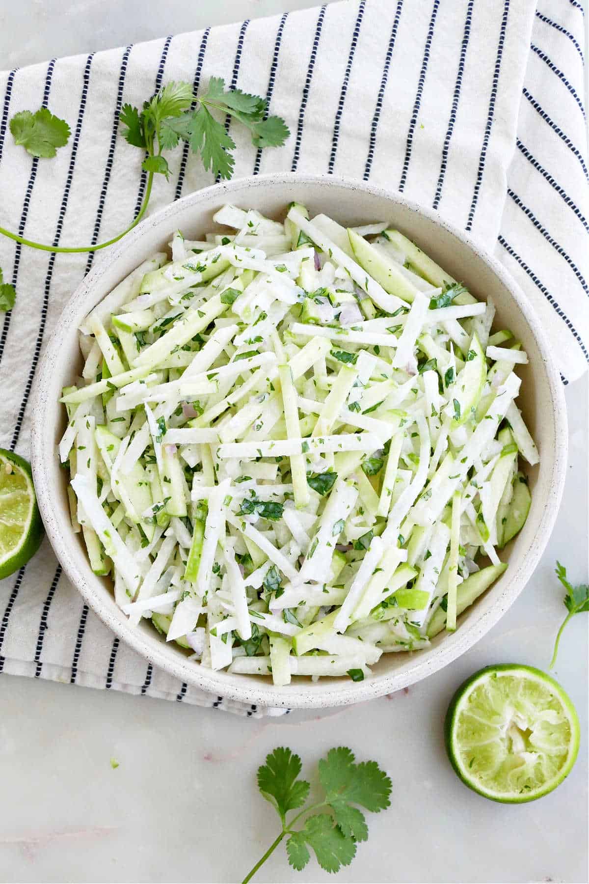 apple jicama slaw in a serving bowl surrounded by garnish and a napkin