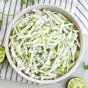 apple jicama slaw in a serving bowl surrounded by garnish and a napkin