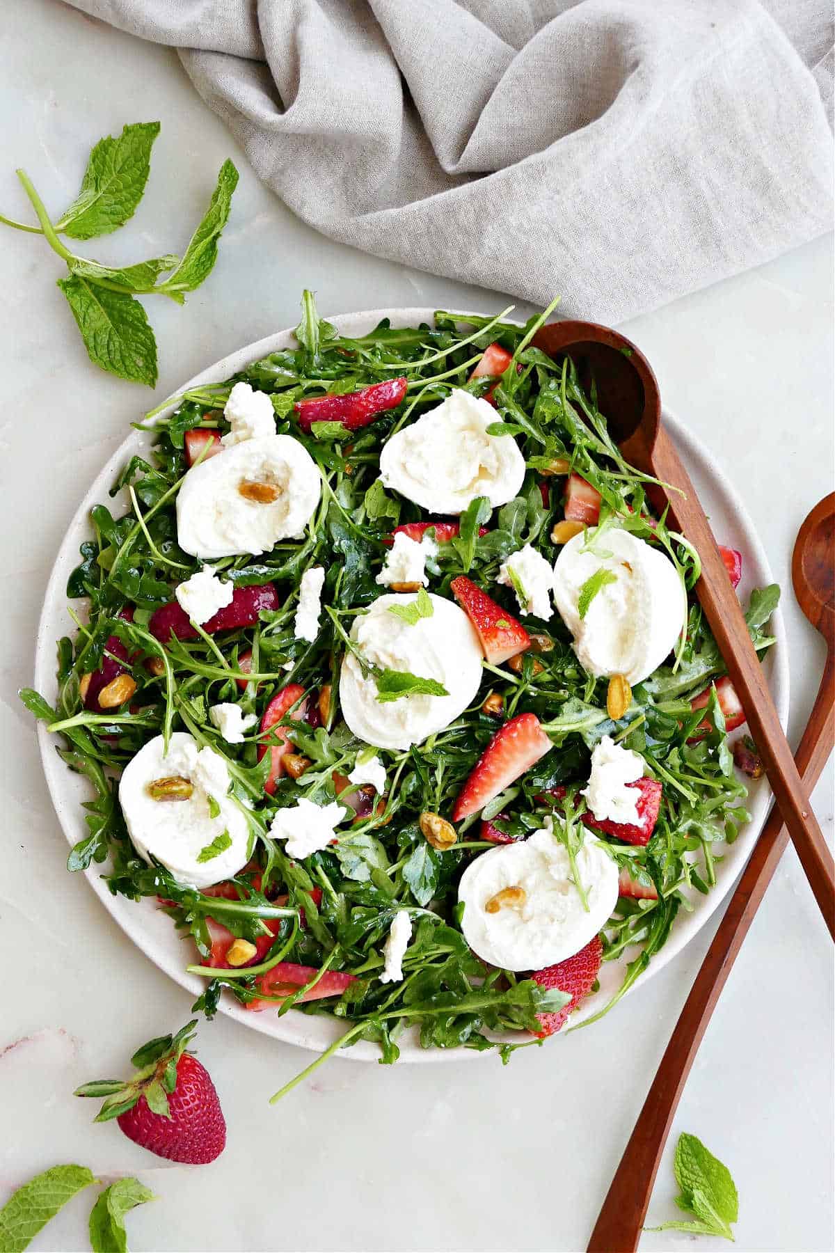arugula salad with burrata and berries on a serving plate with wooden tongs