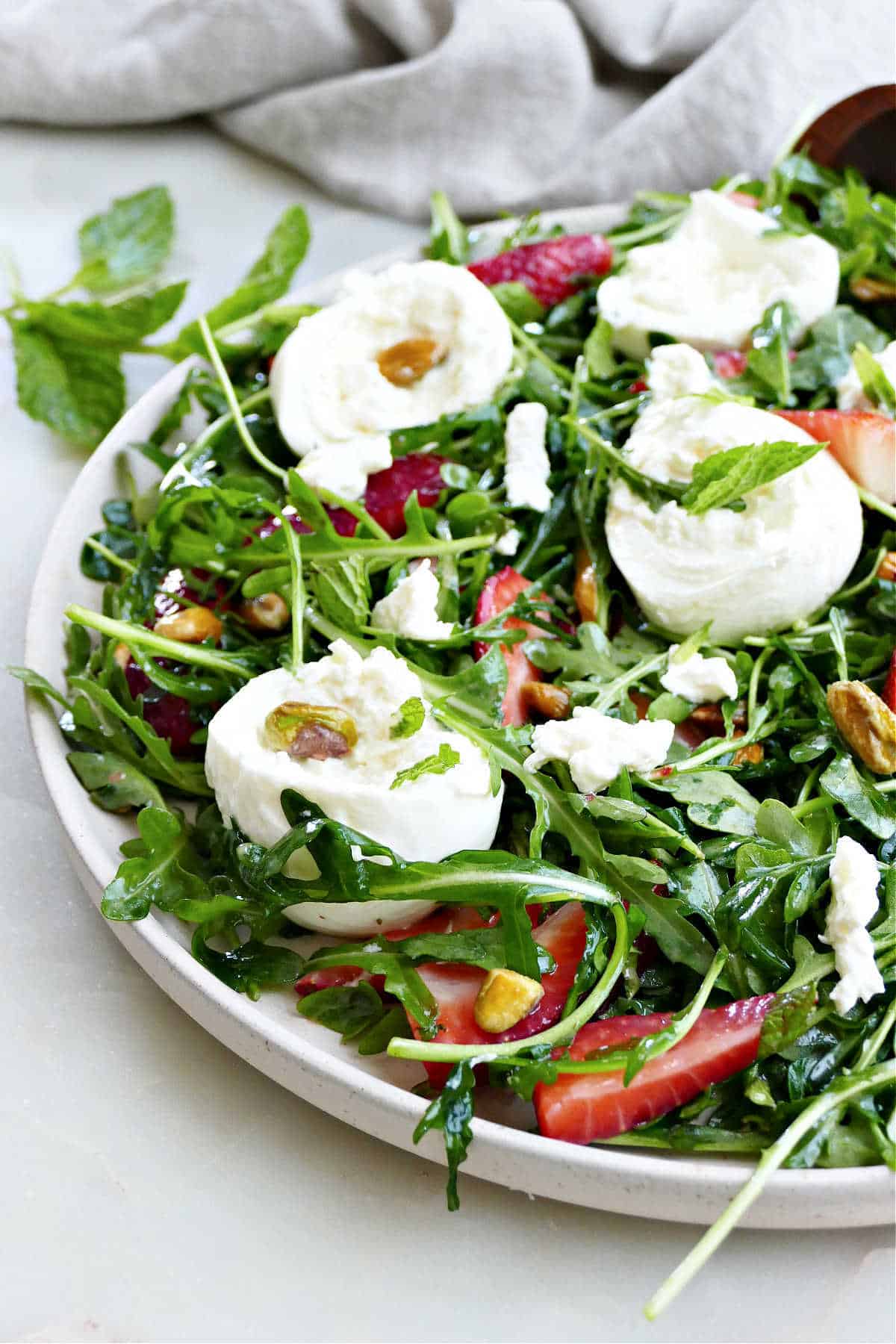 arugula, burrata cheese, berries, and pistachios tossed in dressing on a plate