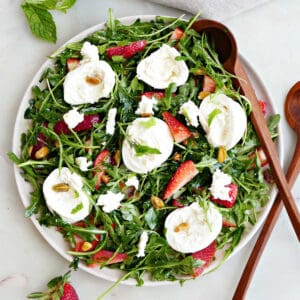 arugula salad with burrata and berries on a serving plate with wooden tongs