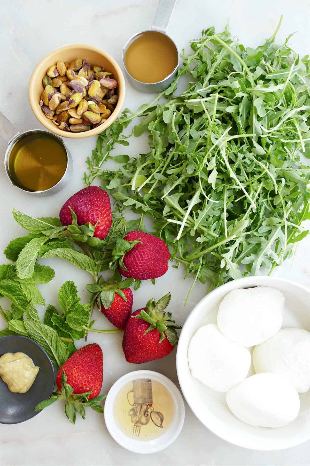 arugula, pistachios, strawberries, burrata, and dressing ingredients next to each other on a counter