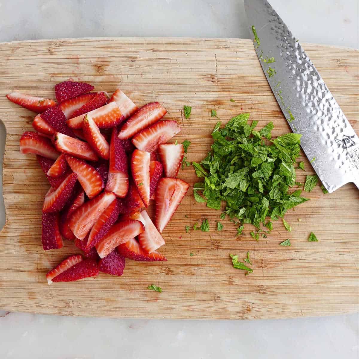 sliced strawberries and chopped mint on a cutting board next to a knife