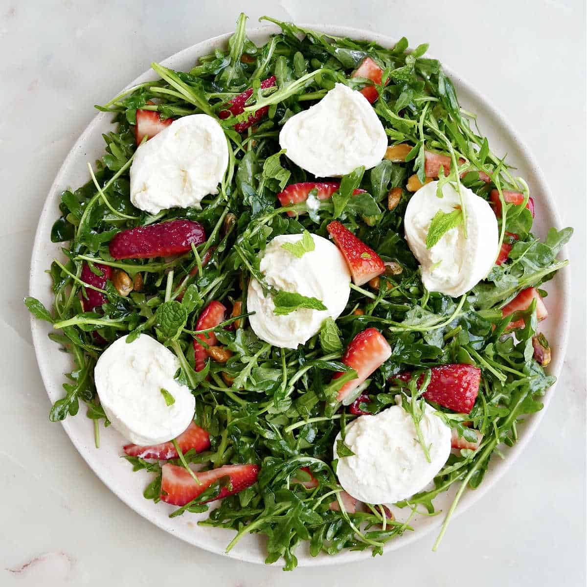 arugula salad with burrata, berries, and pistachios on a serving plate