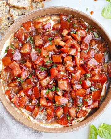 cold bruschetta dip in a serving bowl next to crackers and a napkin