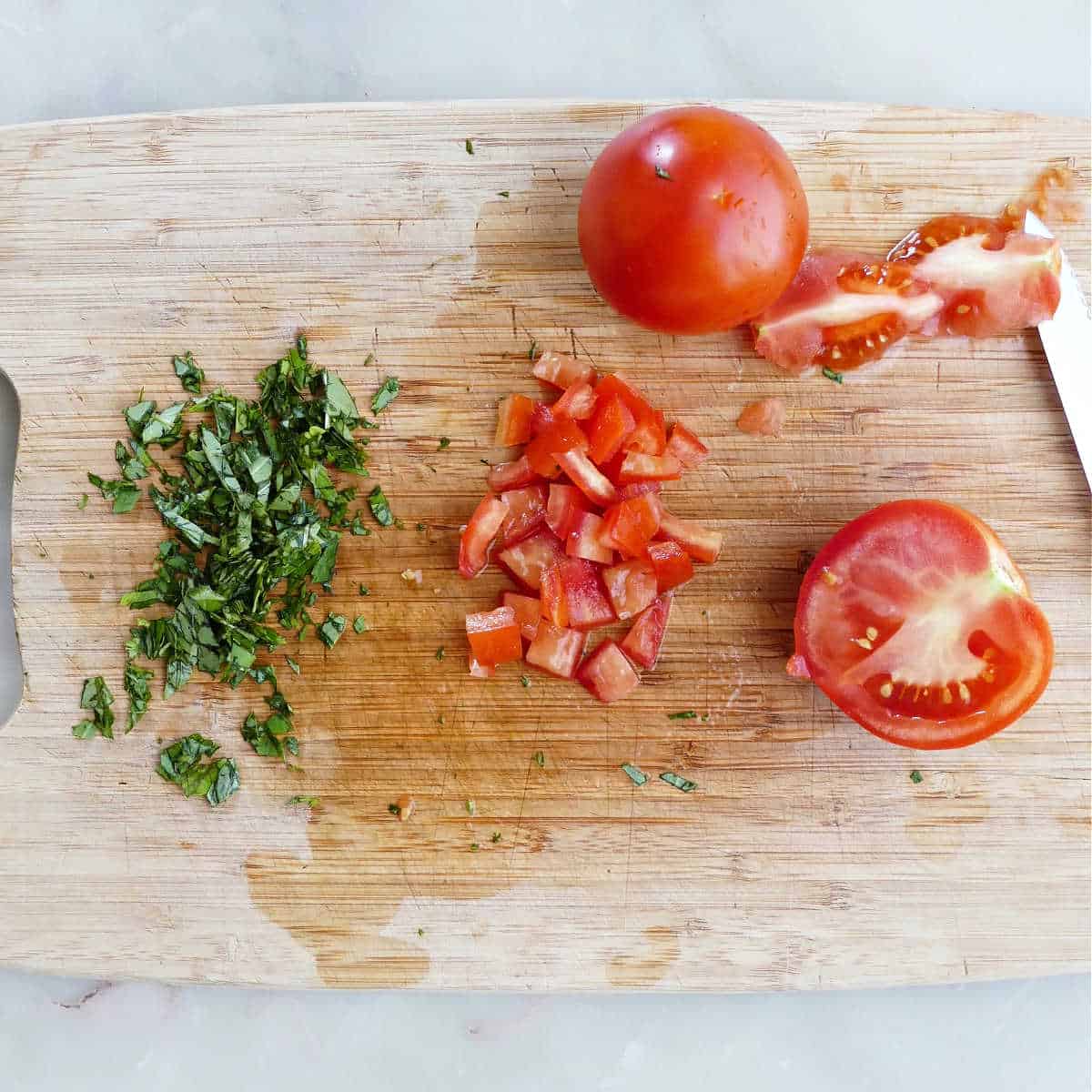 chopped basil and tomatoes on a cutting board next to a knife