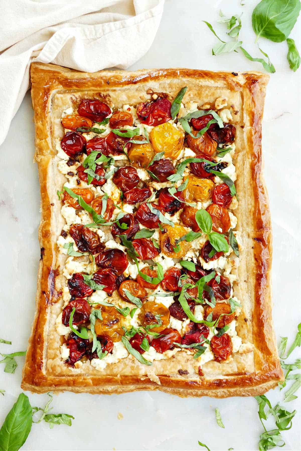 roasted cherry tomato tart on a counter next to basil leaves and a napkin