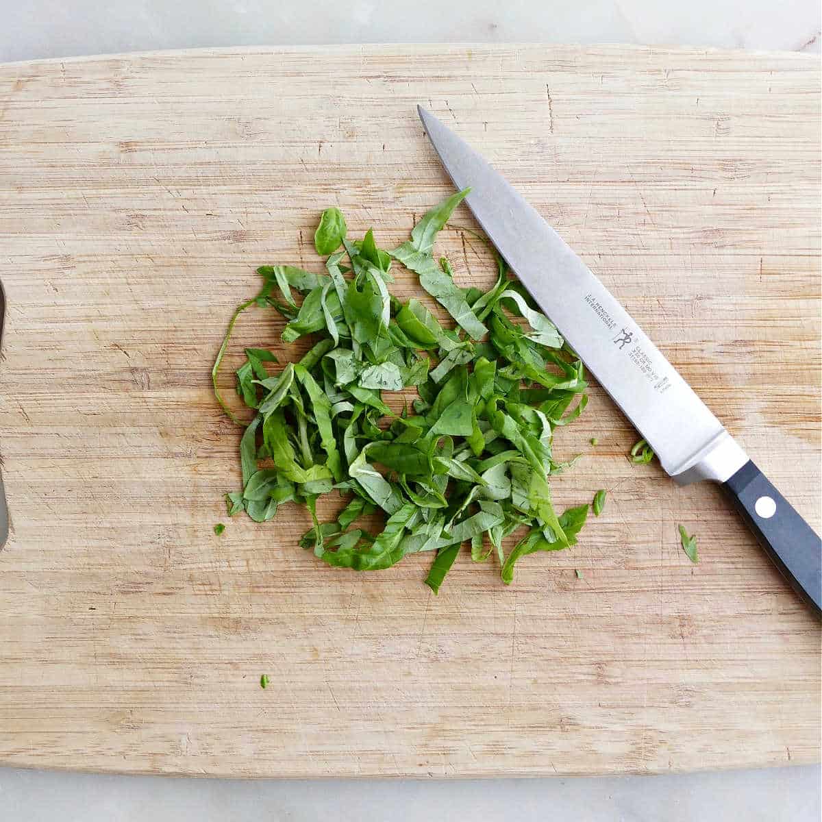 basil cut into chiffonade pieces on a cutting board next to a knife