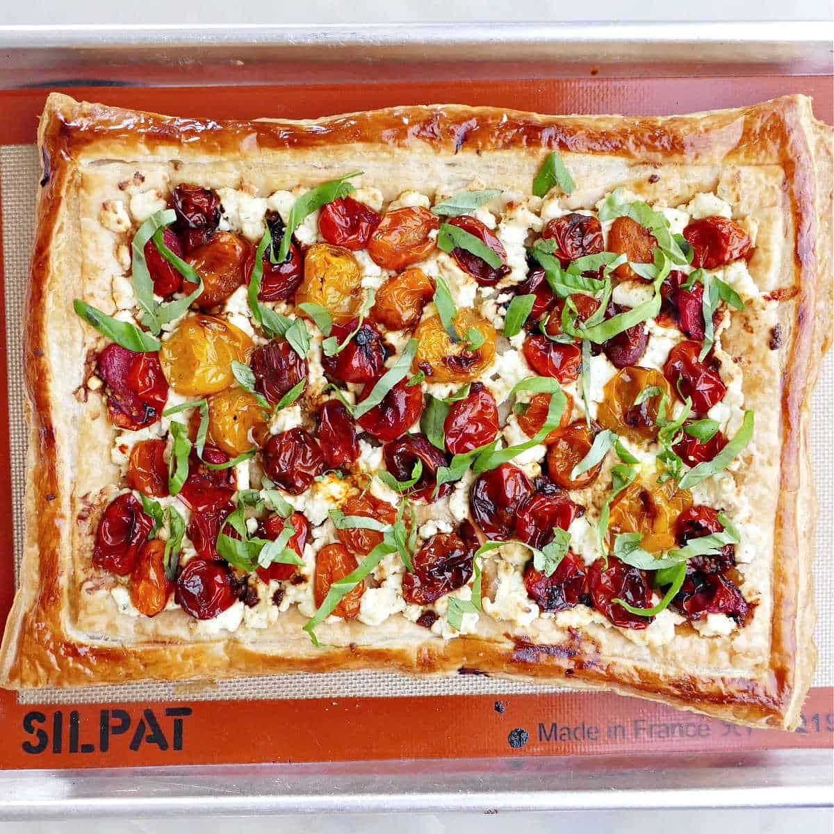 baked puff pastry topped with roasted cherry tomatoes, cheese, and basil on a baking sheet
