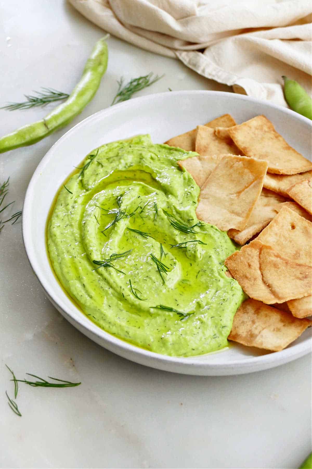 fava bean and dill hummus on a plate next to pita chips