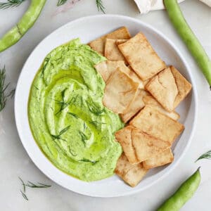 fava bean hummus with dill on a plate next to pita chips