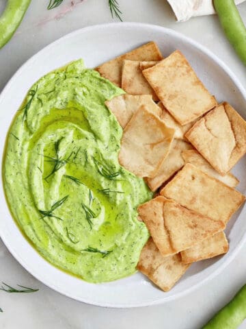 fava bean hummus with dill on a plate next to pita chips