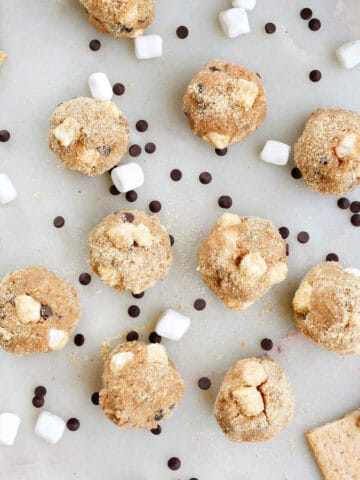 s'mores balls on a counter surrounded by mini marshmallows and chocolate chips