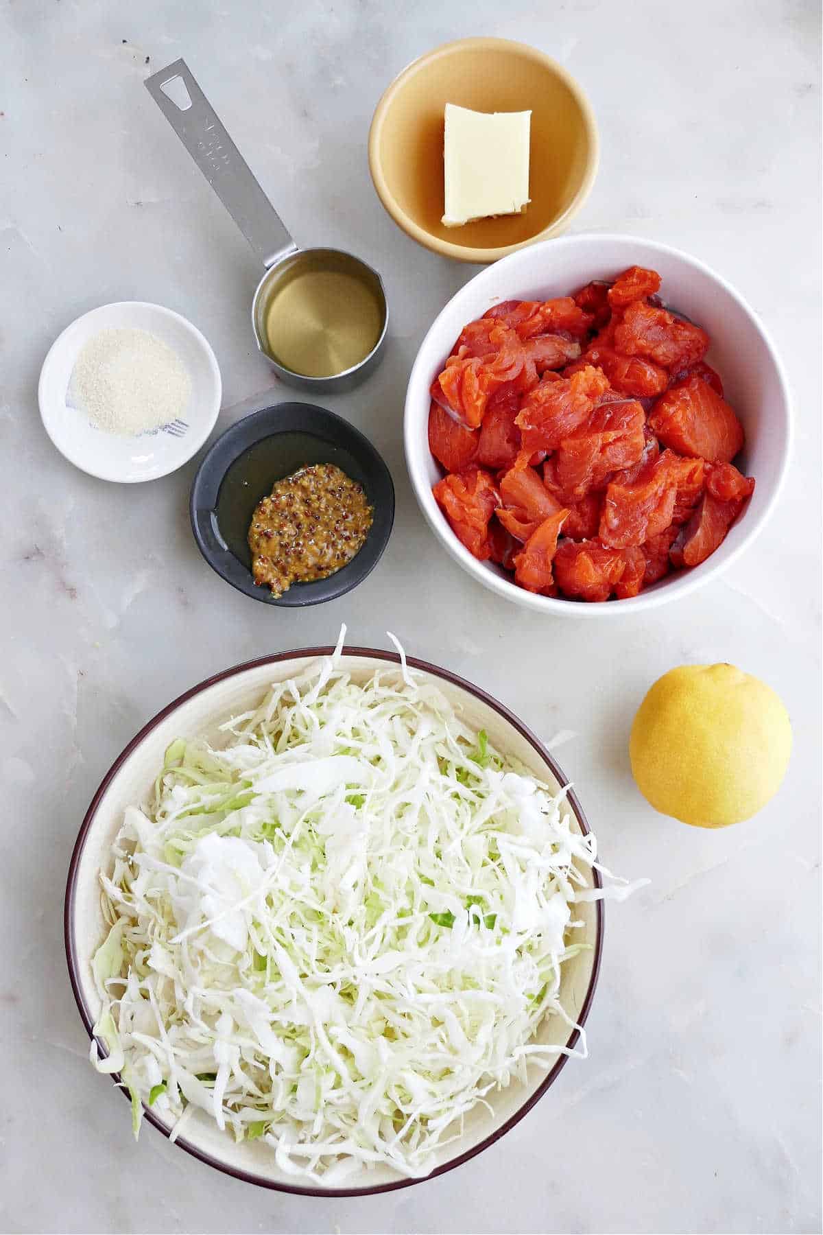 coleslaw, salmon cubes, lemon, olive oil, butter, mustard, and seasonings on a counter