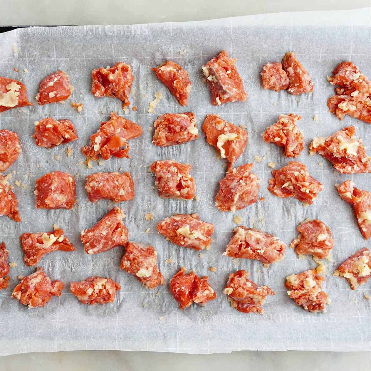 marinated lemon butter salmon bites spread out on a lined baking sheet before going into the oven
