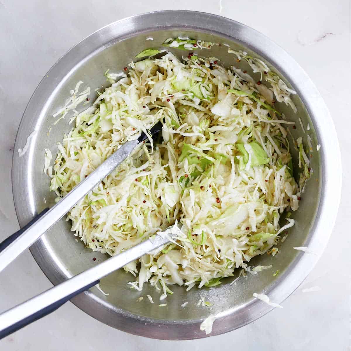 coleslaw mixed with a vinegar dressing in a mixing bowl with tongs