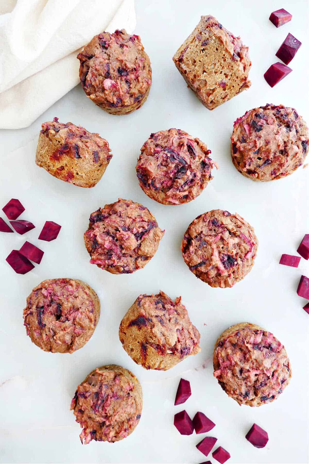11 beet apple muffins spread out on a counter next to cubed beets