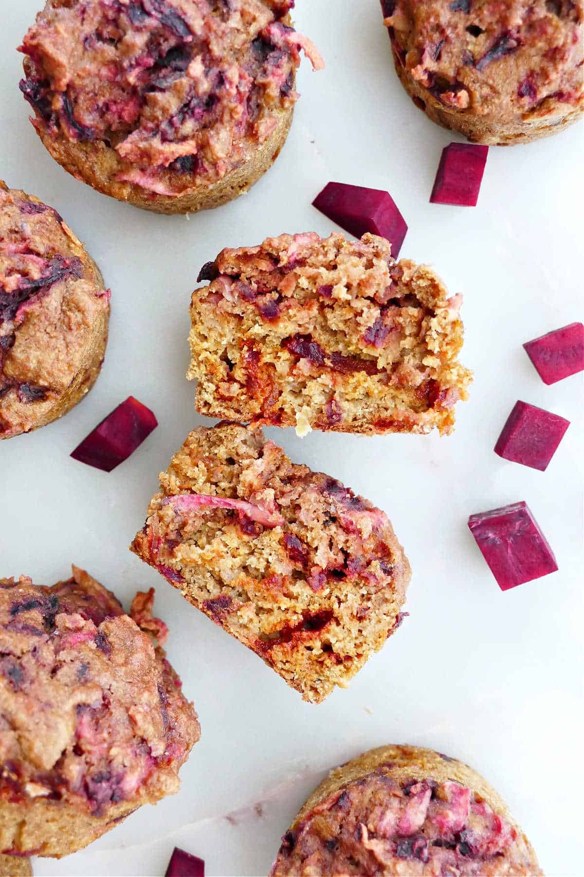 a beet muffin sliced in half on a counter next to other muffins